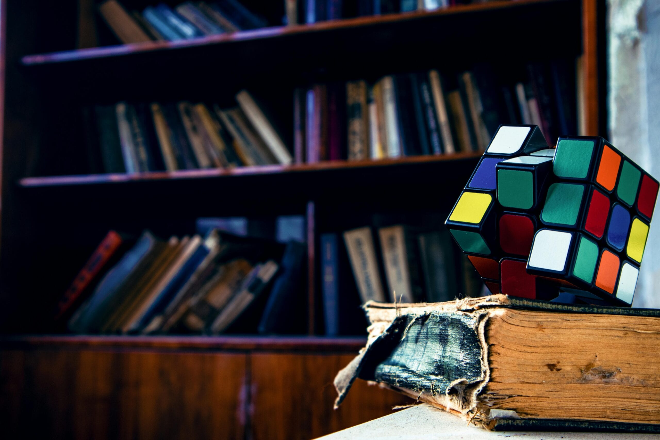 A vivid Rubik's cube resting on a worn book in a cozy library setting.