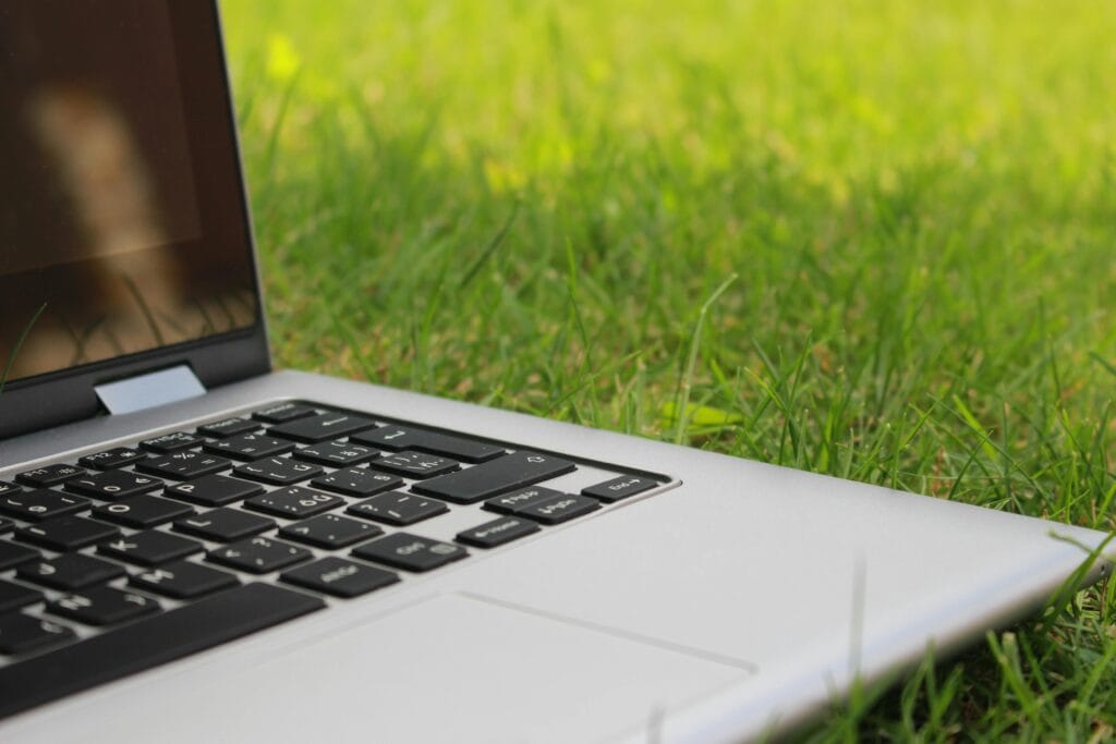 Silver laptop computer on vibrant green grass depicting remote work outdoors in summer.