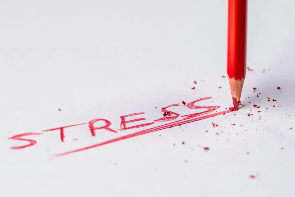 Close-up of a red pencil writing 'stress' on paper, symbolizing pressure and creativity.