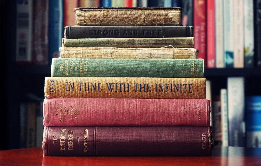 A stack of vintage hardcover books on a wooden table in a cozy library setting.