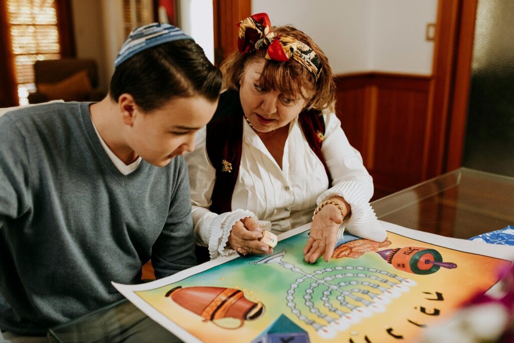 Grandmother and grandson learning about Hanukkah using a colorful board game indoors.