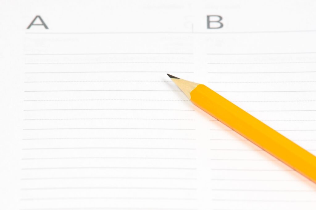 Orange pencil resting on lined paper with columns labeled A and B, ideal for educational themes.